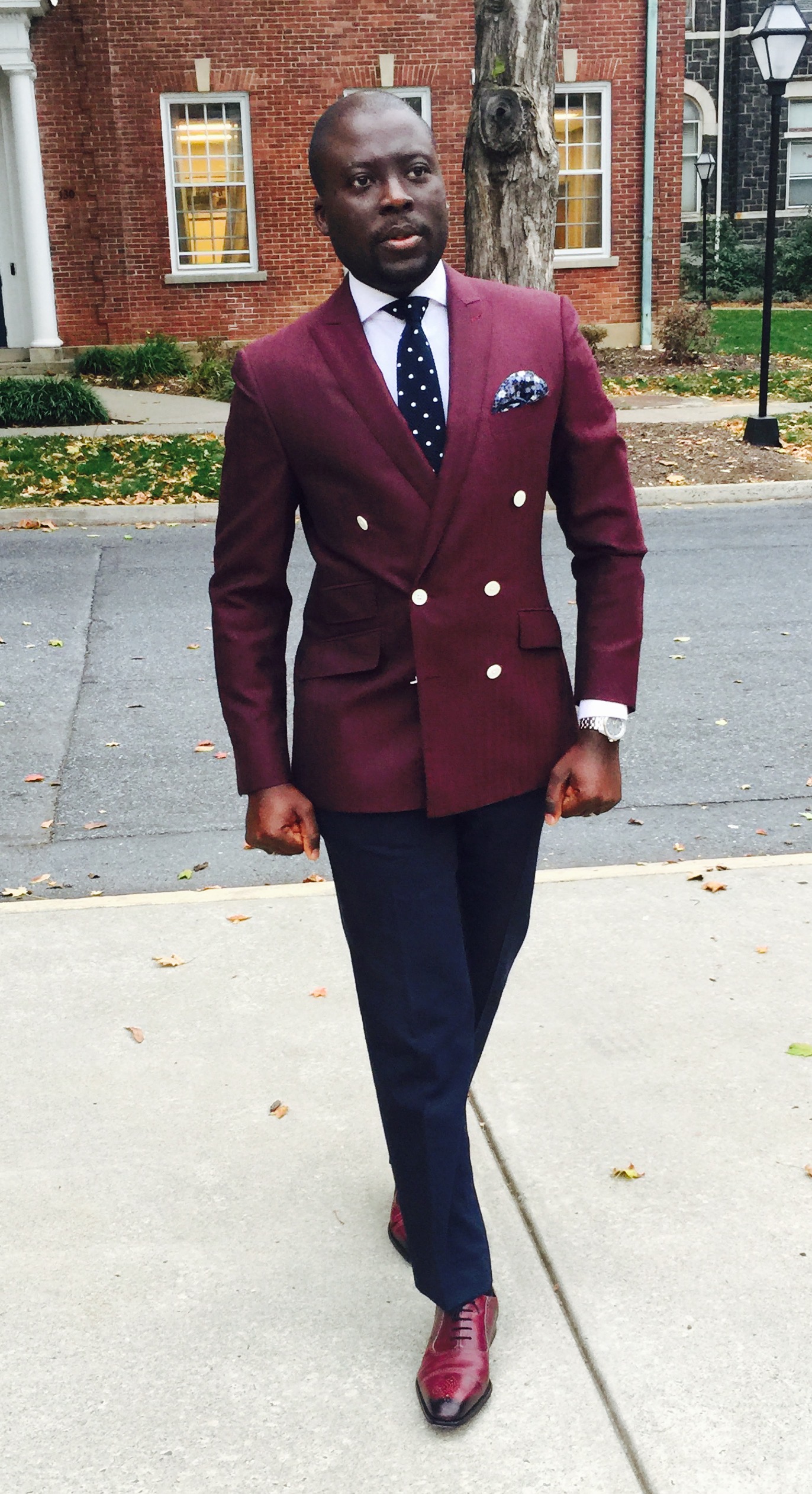 Photo 4 "The Commander": burgundy double-breasted blazer, gold buttons, white shirt, navy polka-dot tie, walking on a sidewalk with autumn leaves