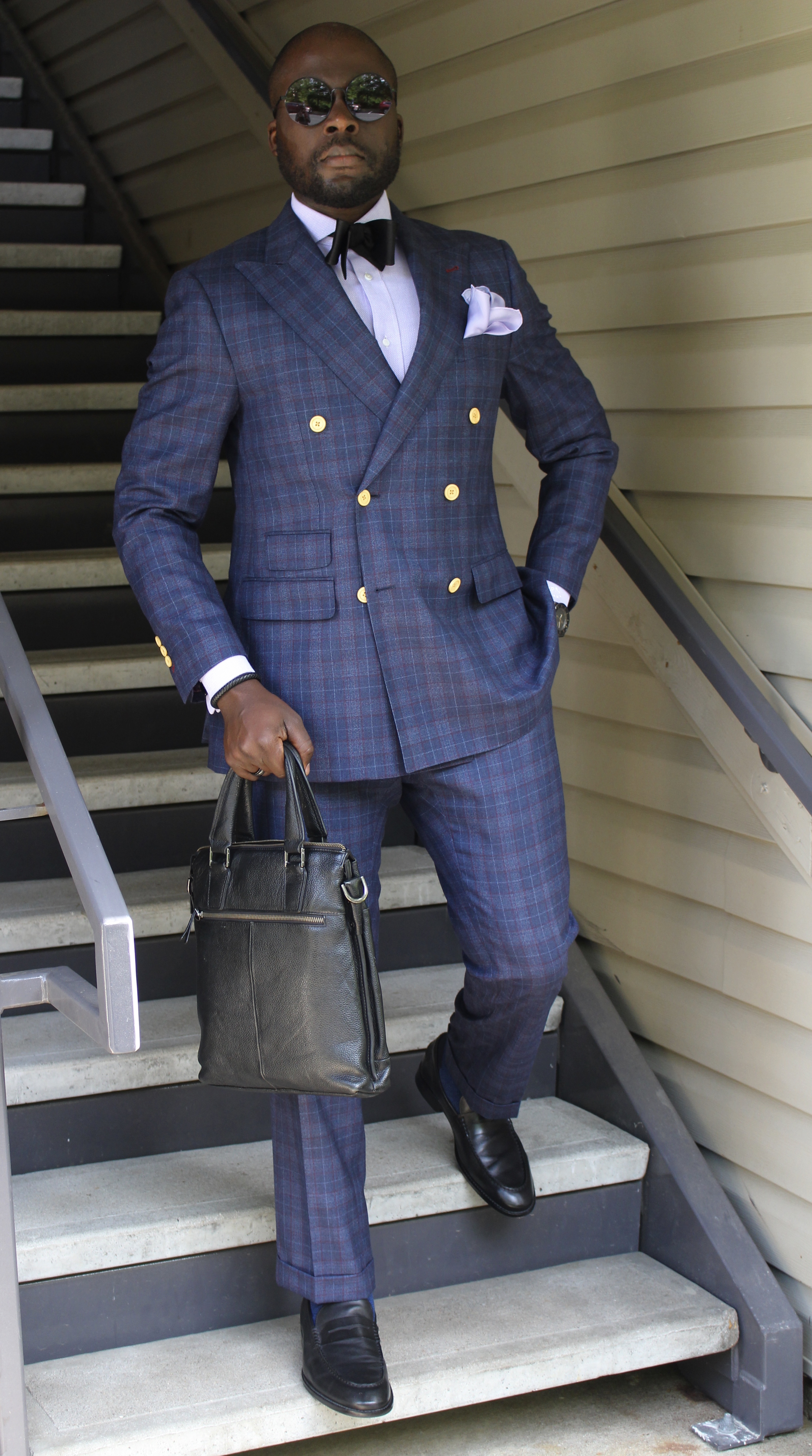 Photo 2 "The Journey": blue plaid double-breasted suit, gold buttons, white shirt, black bow tie, briefcase, on a staircase with round sunglasses